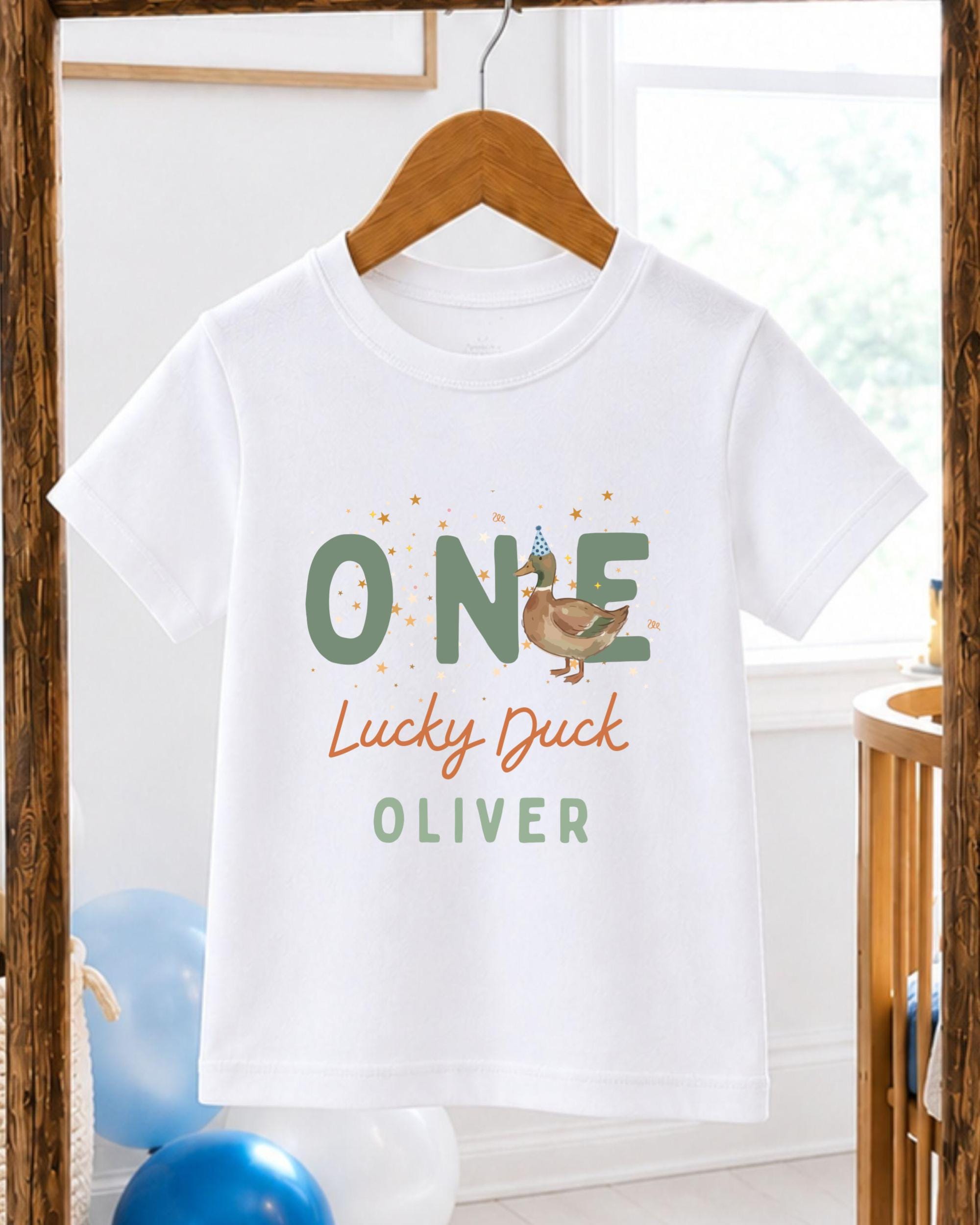 A white t-shirt with a graphic design featuring a cartoon duck and the text "One Lucky Duck Oliver" printed on it.