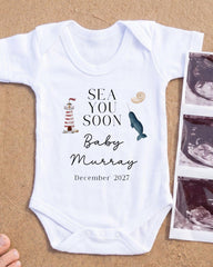 A white onesie with text and illustrations related to a baby announcement, placed on a sandy surface next to a photograph of an Ultrasound image.
