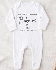 A white onesie with text printed on it, indicating that the family is growing and that a baby is due for Christmas in 2026.