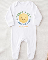 A white onesie with a smiley face design and text printed on it.