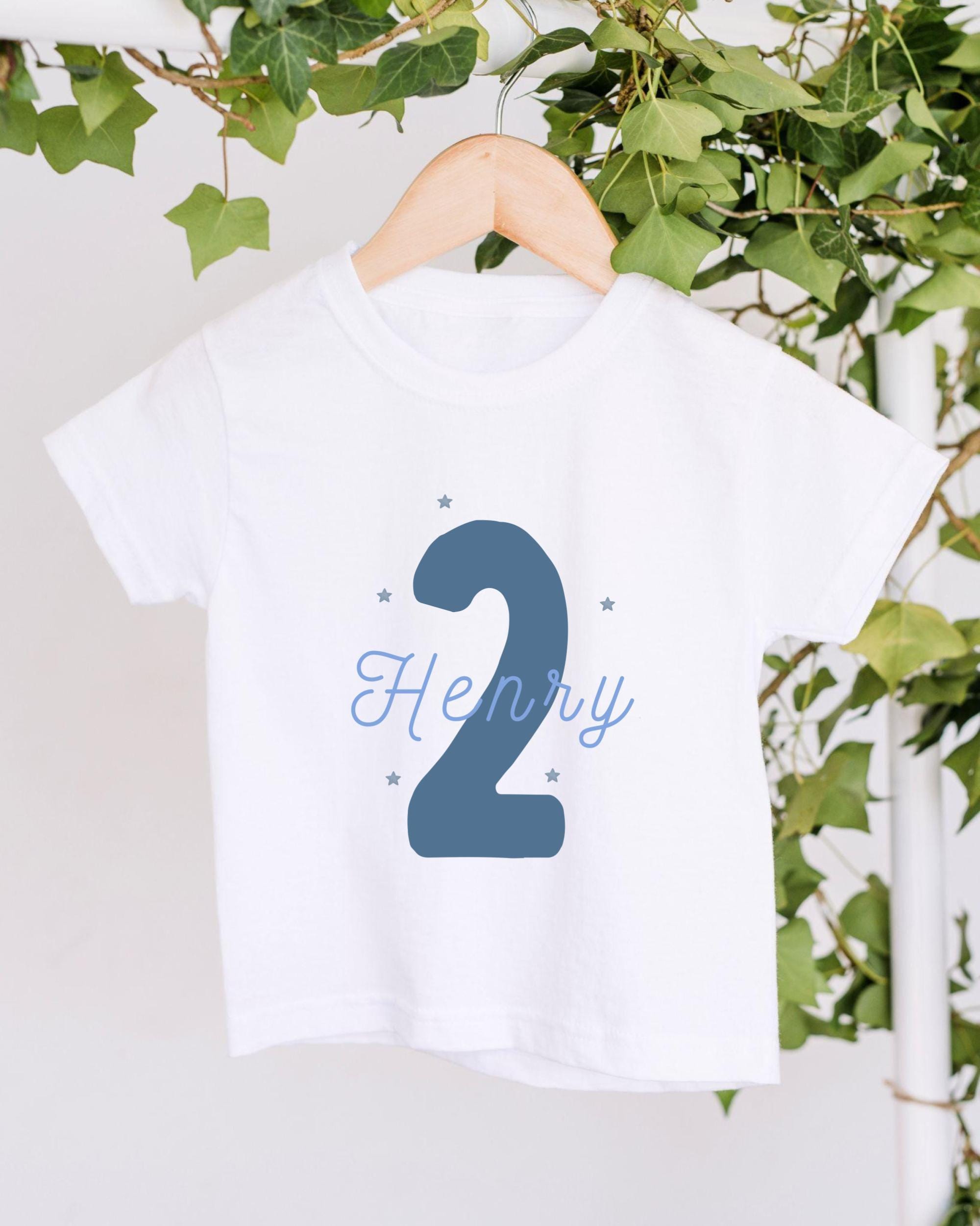 A white t-shirt with a blue number "2" and the name "HENRY" printed on it, hanging on a wooden hanger.