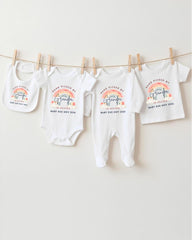 A collection of baby clothes, including onesies and bibs, hanging on a clothesline.