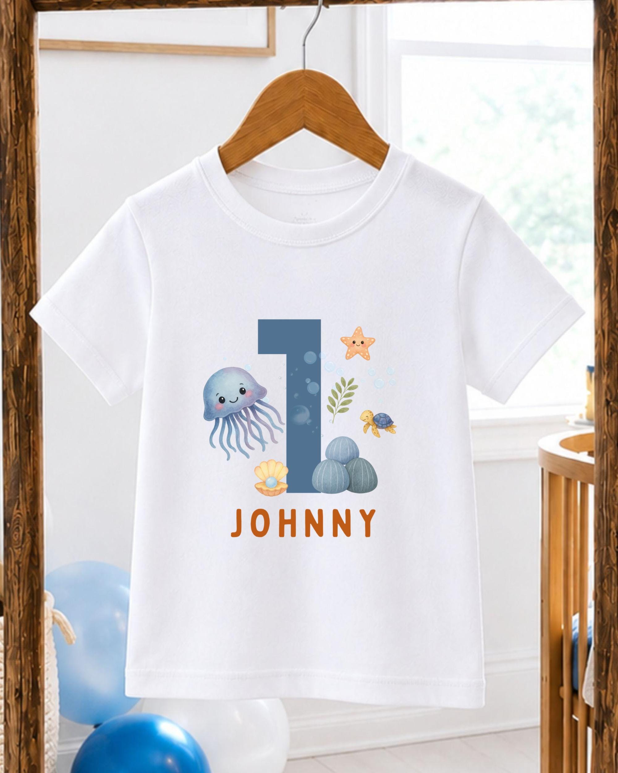 A white t-shirt with a graphic design featuring a blue jellyfish, a starfish, and other sea creatures, along with the text "JOHNNY" printed on it.