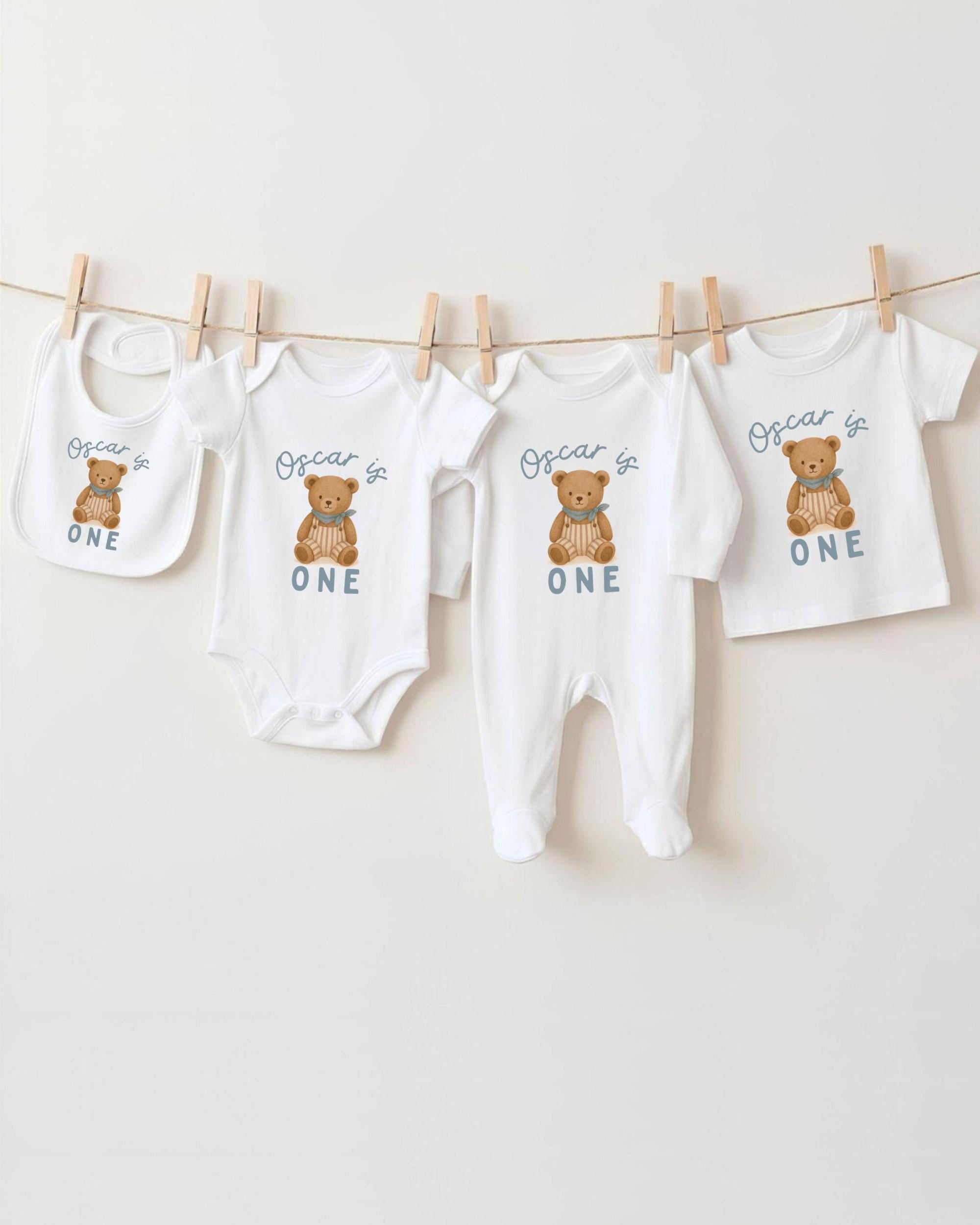 A collection of baby clothes, including onesies and pajamas, with the text "Oscar is ONE" printed on them.