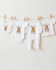 A collection of baby clothes, including onesies and pajamas, with the text "Oscar is ONE" printed on them.