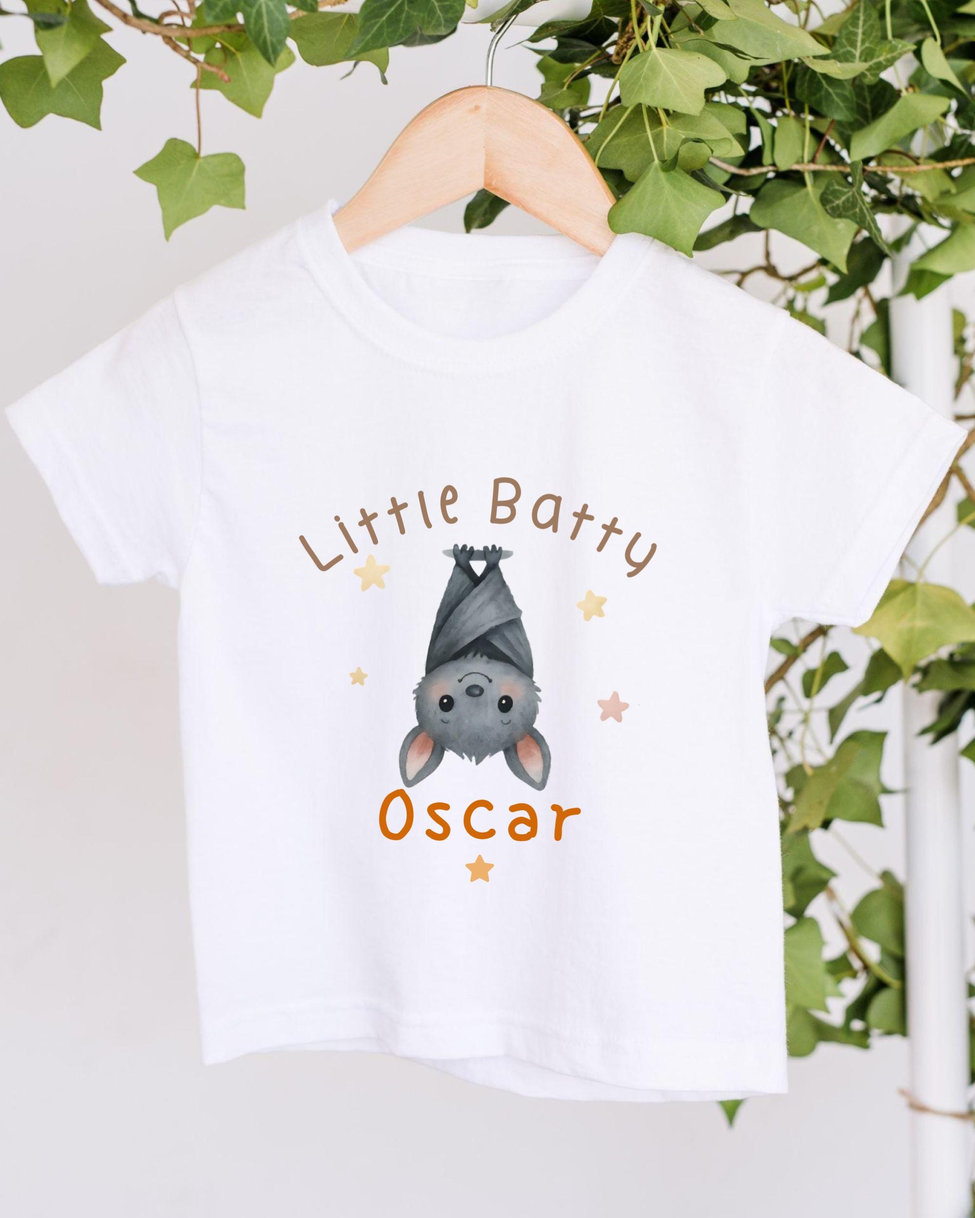 A white t-shirt with a cartoon bat hanging upside down and the text "Little Batty Oscar" printed on it.