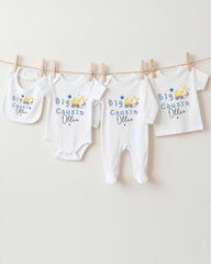 A row of four white baby clothes with blue and yellow construction-themed designs hanging on a clothesline.