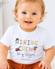 A smiling baby wearing a white t-shirt with colorful text and graphics.