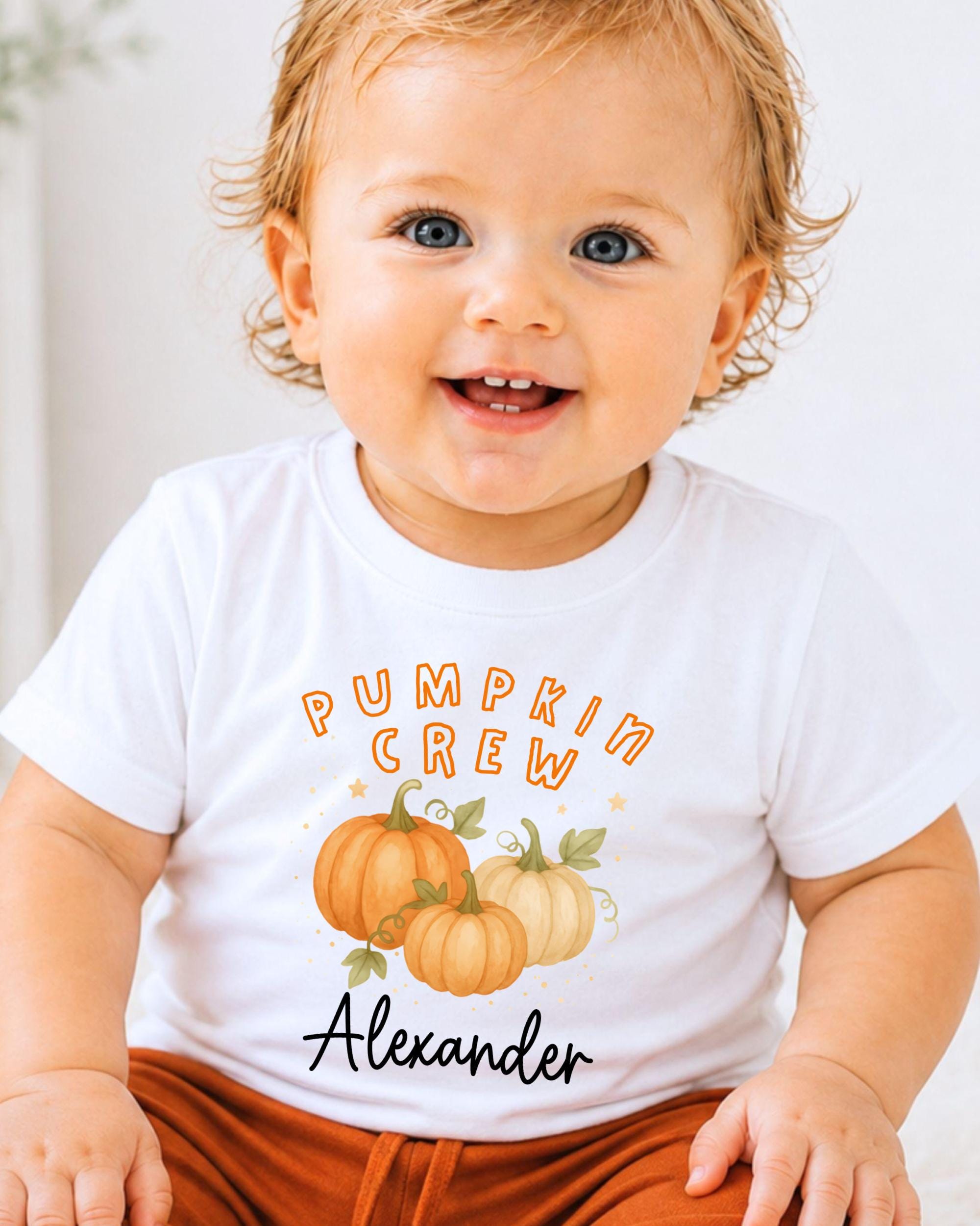 A smiling baby boy wearing a white t-shirt with a pumpkin graphic and the text "Pumpkin Crew Alexander" printed on it.