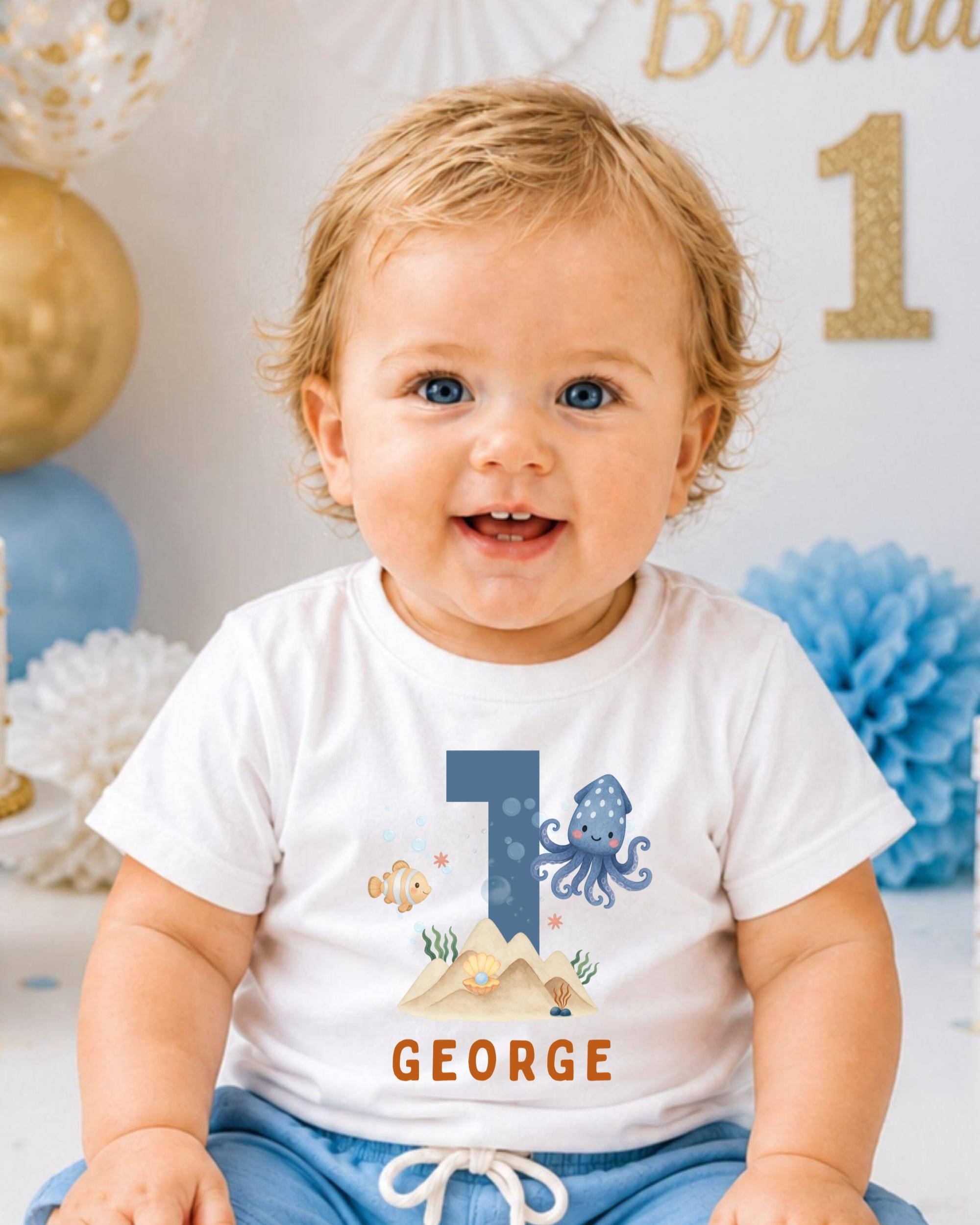 A smiling baby boy wearing a white t-shirt with a graphic of an octopus and the name "GEORGE" printed on it.