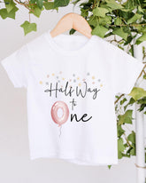 A white t-shirt with a graphic design and text printed on it, hanging on a wooden hanger.