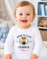 A smiling baby boy wearing a white onesie with a tennis-themed design.