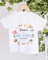 A white t-shirt with a printed design featuring various summer-themed illustrations, including a beach, palm tree, umbrella, and other beach-related objects.