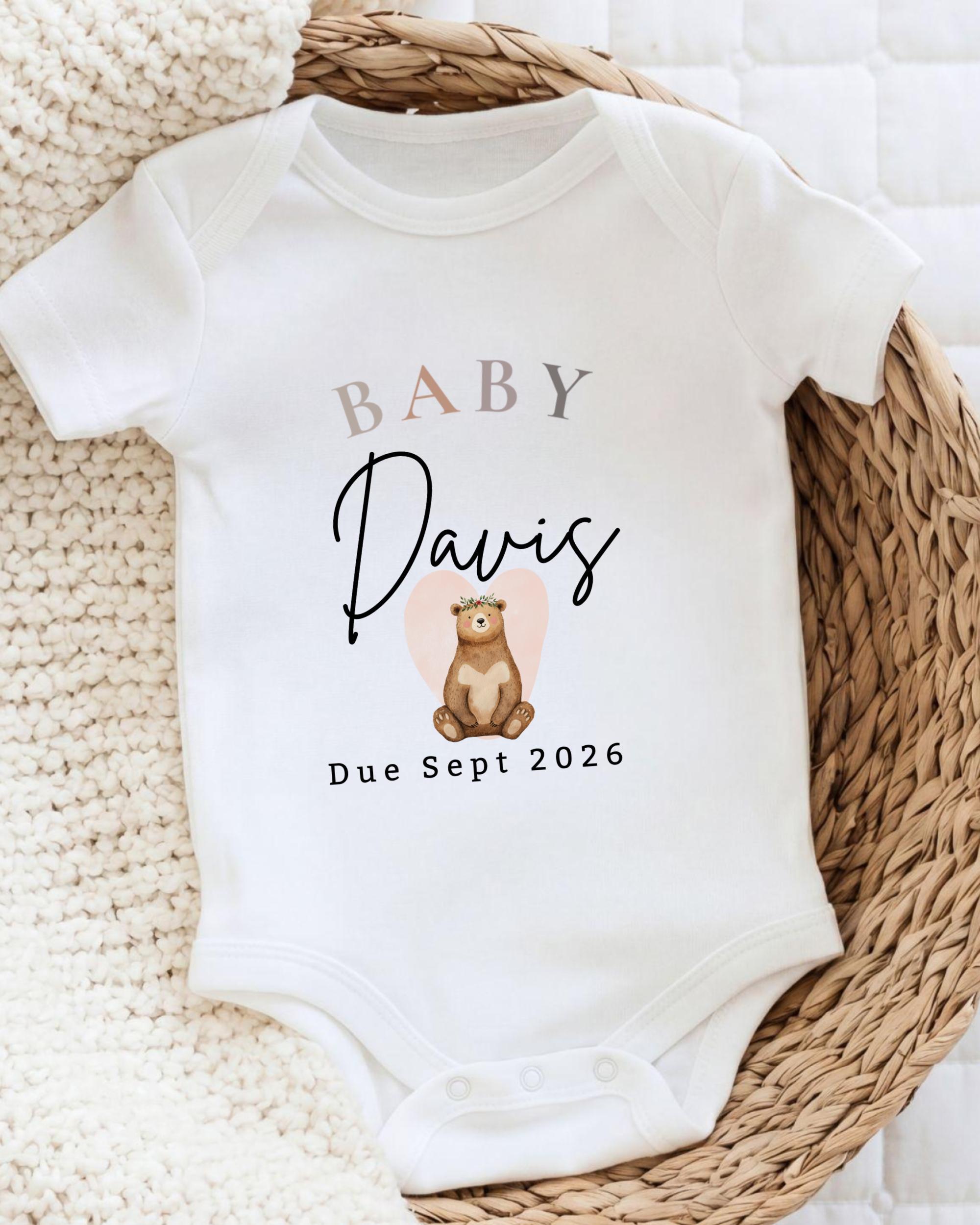 A white baby onesie with the text "BABY Davis Due Sept 2026" printed on it, along with an illustration of a bear.