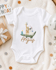 A white onesie with a giraffe and a birthday cake printed on it, along with a "Happy Birthday" sign and a birthday balloon.
