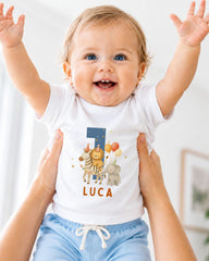 A smiling baby wearing a white t-shirt with a personalized number 1 and animal designs, being held up by someone's arms.