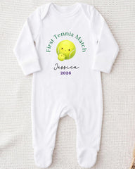 A white onesie with a tennis ball design and text printed on it.