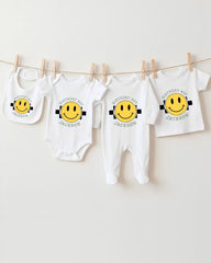 A collection of white baby clothes with yellow smiley faces printed on them, hanging on a clothesline.