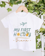 A white t-shirt with a graphic design that says "My first holiday - Diana" and features a plane, sun, and palm trees.