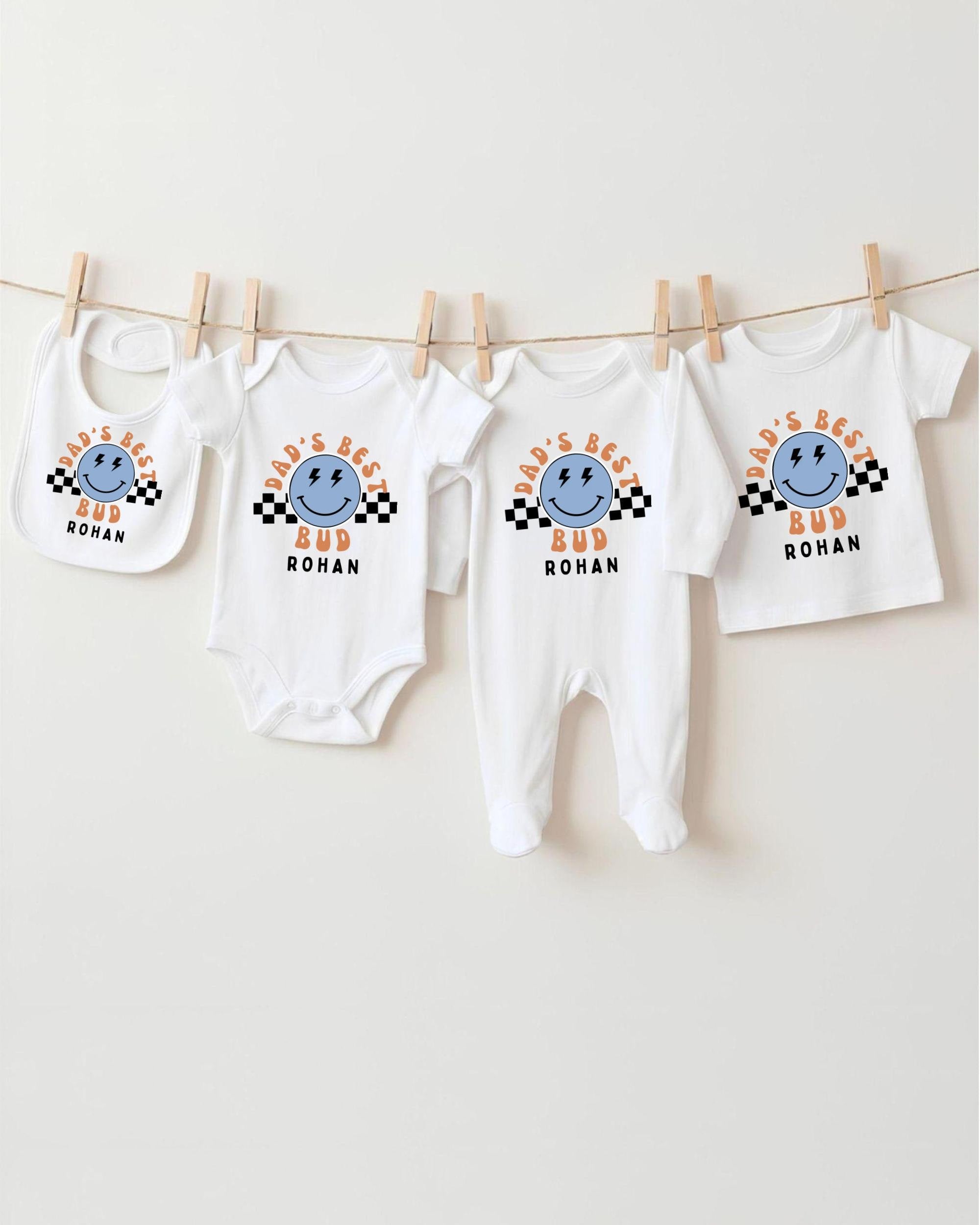 A collection of four white baby clothes, including onesies and bibs, hanging on a clothesline.