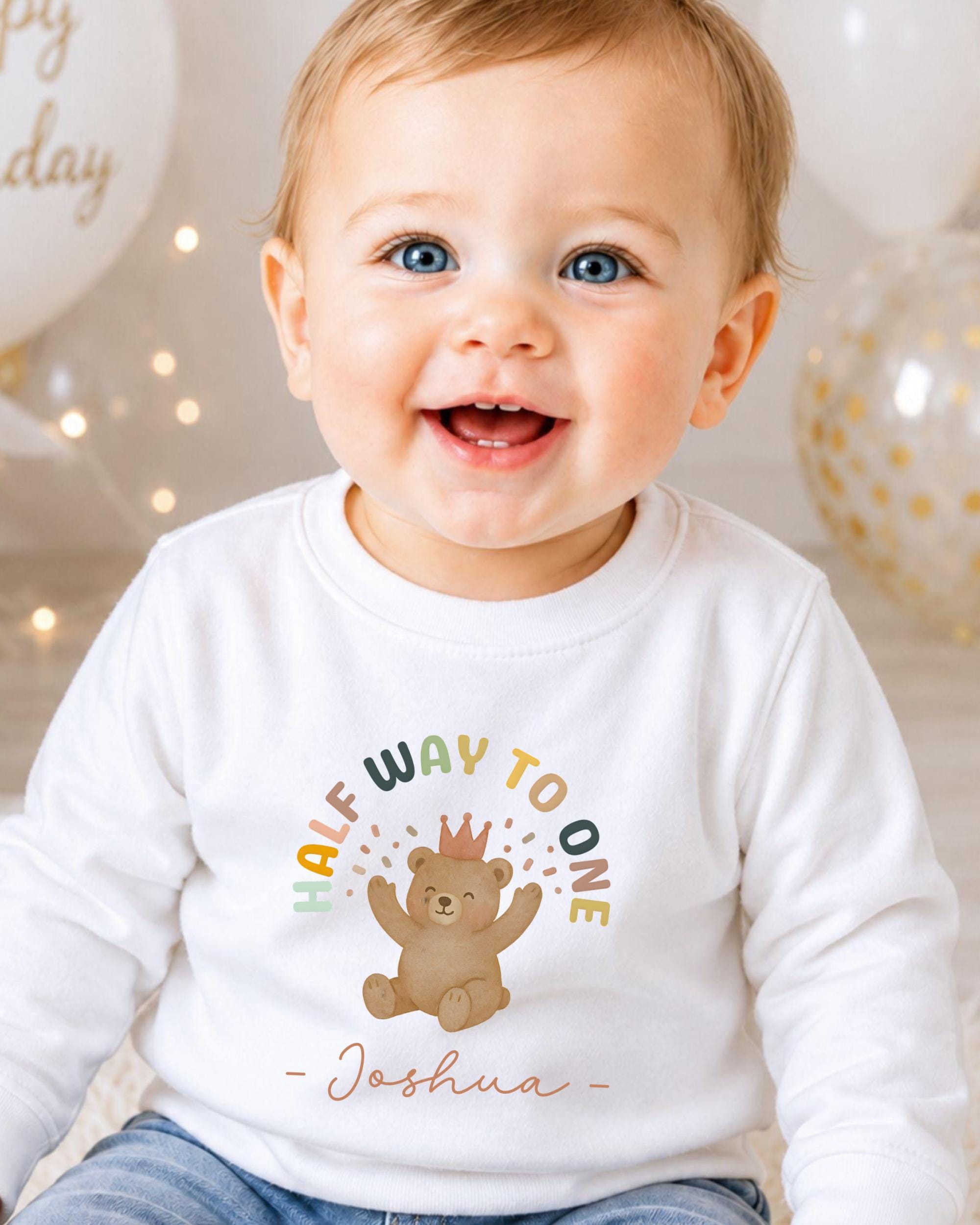 A smiling baby boy wearing a white shirt with a teddy bear graphic and the text "Half Way to One" and " Joshua" printed on it.