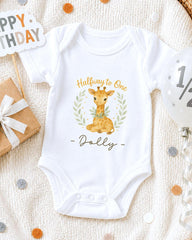A white onesie with a giraffe design and the text "Halfway to One Dolly" printed on it, along with a "Happy Birthday" sign and confetti.