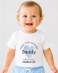 A smiling baby boy wearing a white t-shirt with a personalized message and a heart graphic.