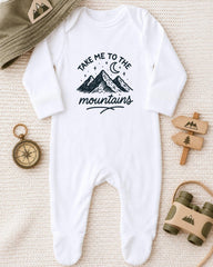A white onesie with a mountain and starry night sky design, along with a compass, a hat, and a pair of binoculars, all arranged on a beige surface.
