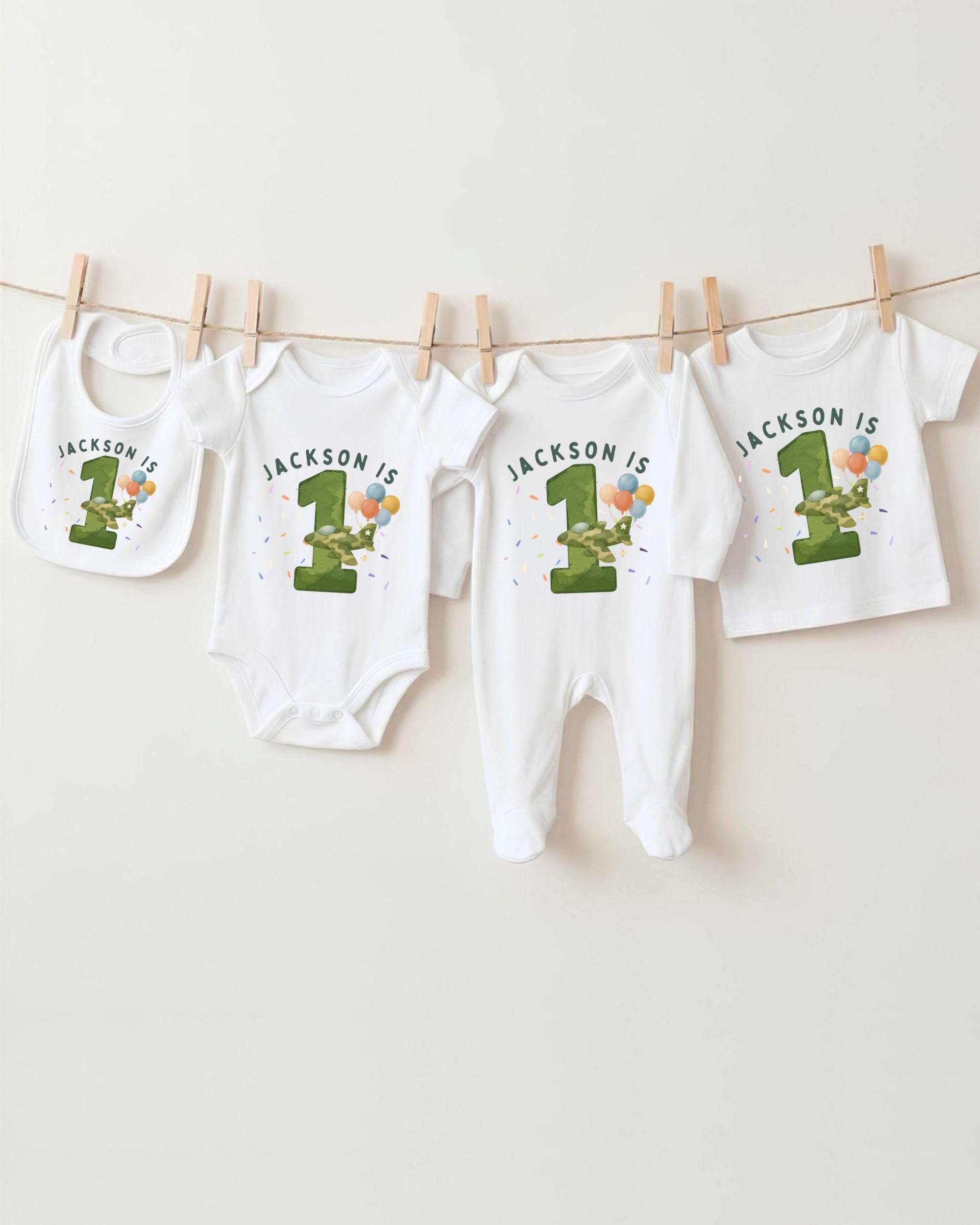 A collection of white baby clothes, including onesies and bibs, with the text "JACKSON IS" printed on them. The clothes are hanging on a clothesline, with the first and third items being the largest.