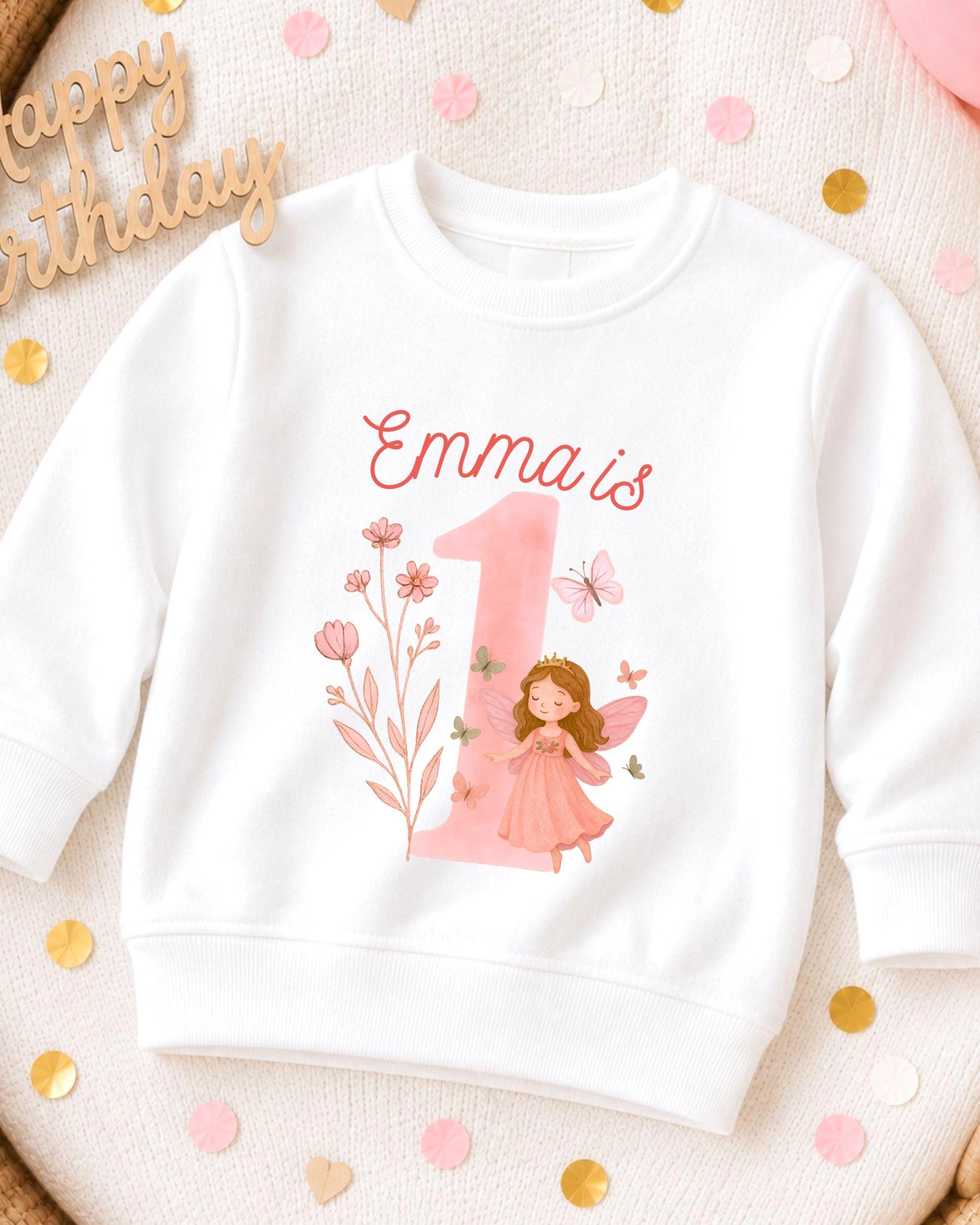A white sweatshirt with a pink fairy and the number 1 printed on it, surrounded by confetti.