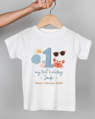A white t-shirt with a graphic design featuring a number 1, sunglasses, a crab, and text that says "my first holiday - Jack - Rome, February 2028".