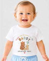A smiling baby boy wearing a white t-shirt with a birthday message and illustrations of bears.