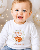 A smiling baby boy wearing a white long-sleeved shirt with a graphic of a fox and the text "Halfway to One" and "Knox" printed on it.