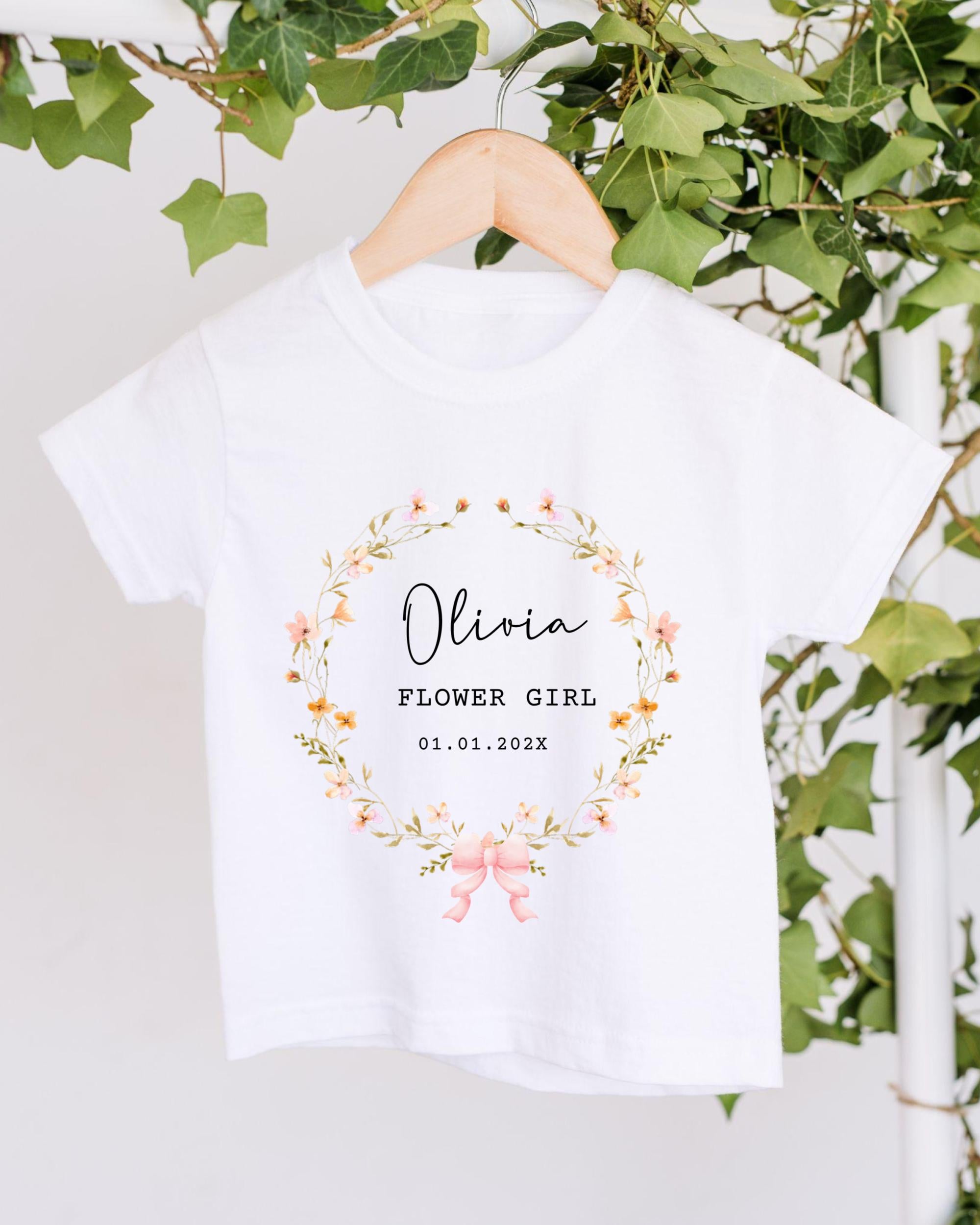 A white t-shirt with a floral wreath design and text printed on it, hanging on a wooden hanger.