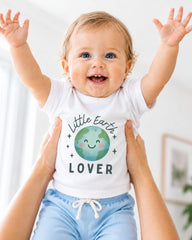 A smiling baby wearing a white shirt with a green and blue design and the text "Little Earth Lover" is being held up by someone's arms.