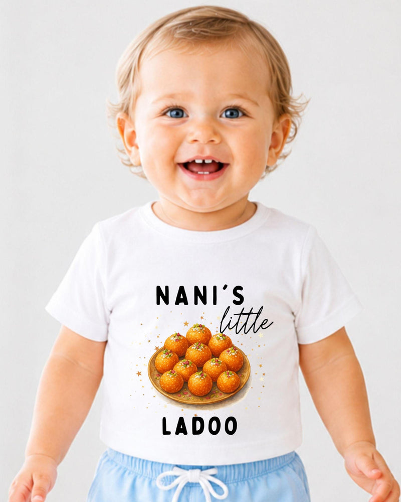 A smiling baby wearing a white t-shirt with a graphic of a plate of oranges and the text "NANI'S LITTLE LADOO" printed on it.