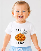 A smiling baby wearing a white t-shirt with a graphic of a plate of oranges and the text "NANI'S LITTLE LADOO" printed on it.