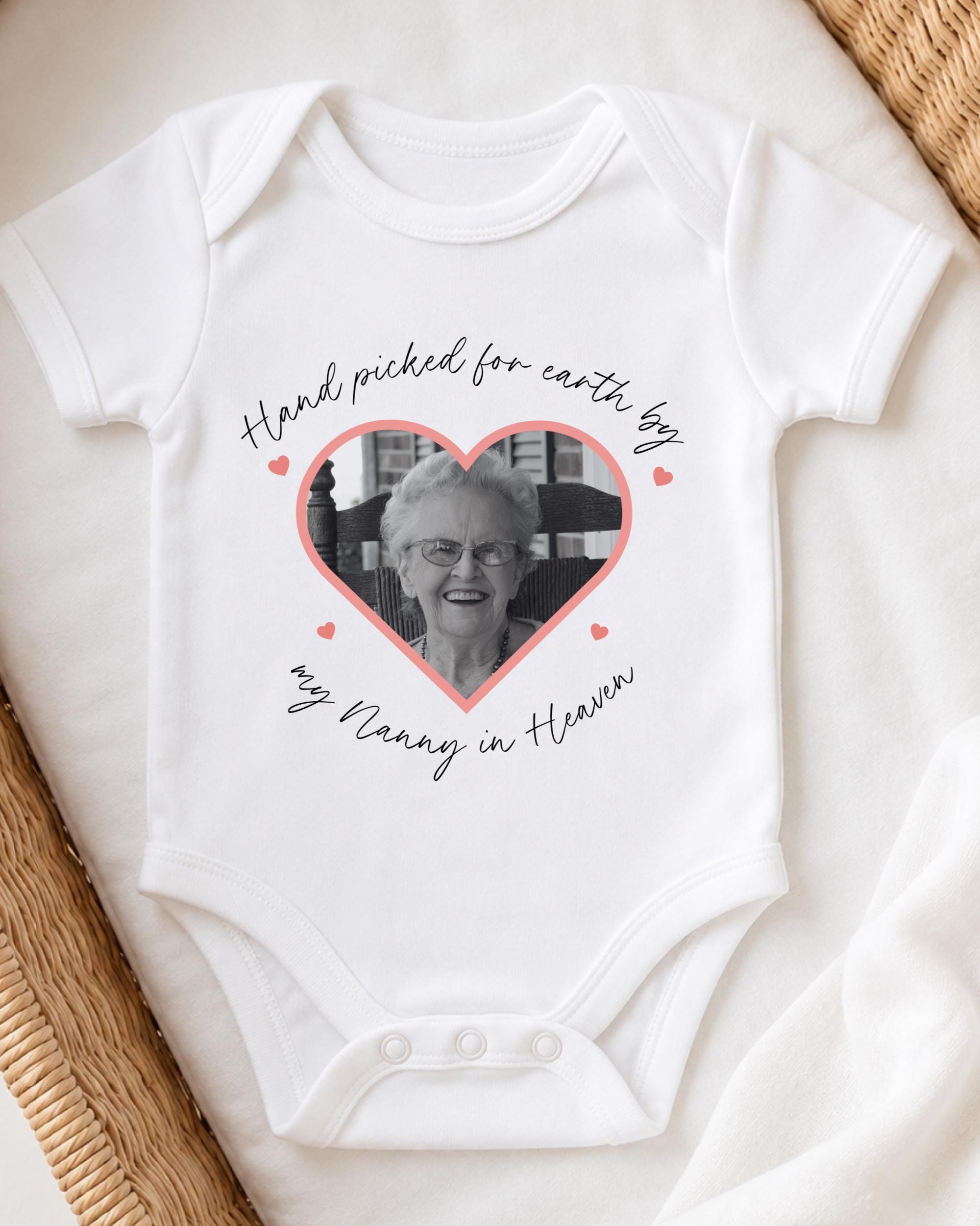 A white baby onesie with a heart-shaped photo of an elderly woman and the text "Hand picked for earth by my Nancy in Heaven" printed on it.