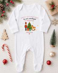 A white onesie with a Christmas-themed design, including a nutcracker, presents, and a tree, is displayed on a white surface alongside various Christmas decorations and gifts.