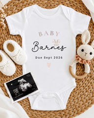 a baby announcement, including a white onesie with the text "BABY Barnes Due Sept 2026", a crocheted bunny toy, and a black and white baby photo.