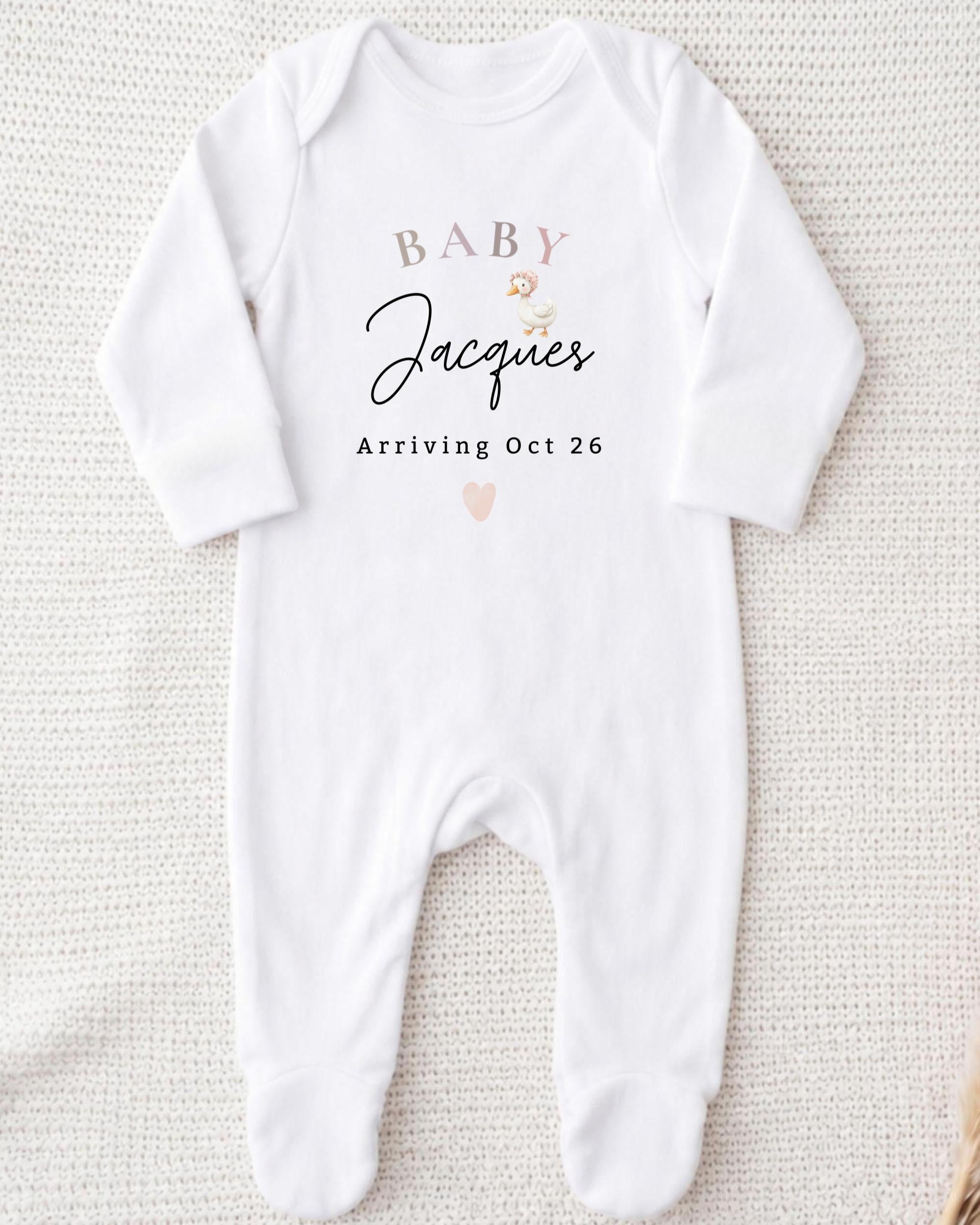 A white onesie with text and a heart graphic, indicating the arrival of a baby named Jacques.