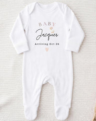 A white onesie with text and a heart graphic, indicating the arrival of a baby named Jacques.