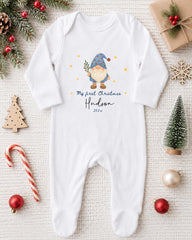 A white onesie with a gnome design and text, surrounded by Christmas decorations and ornaments.