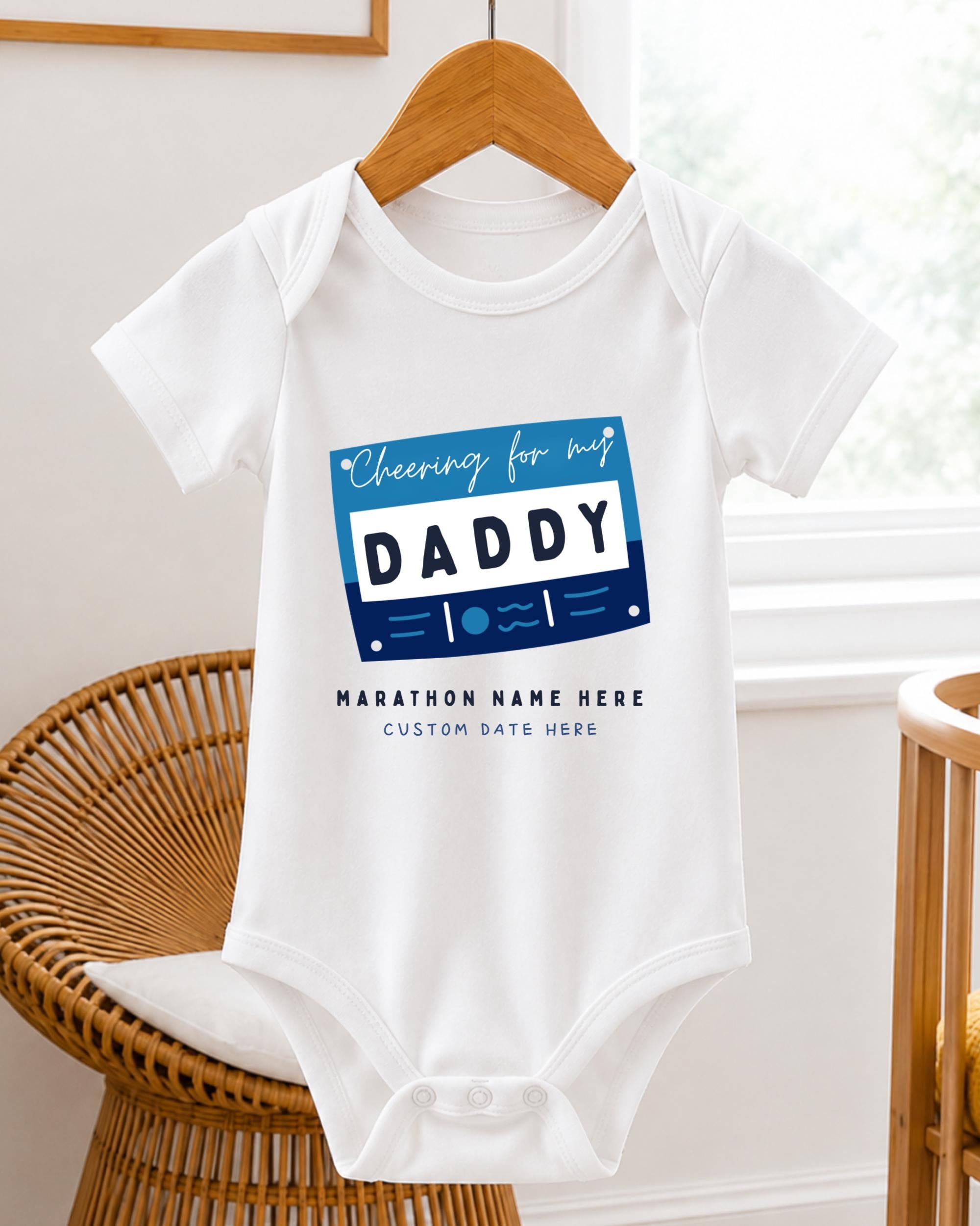 A white baby onesie with a graphic design on it, hanging on a wooden hanger.