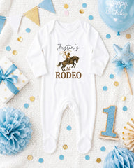A baby onesie with the text " Justin's Rodeo" printed on it, surrounded by various baby-themed items such as a blue balloon, a star, and confetti.