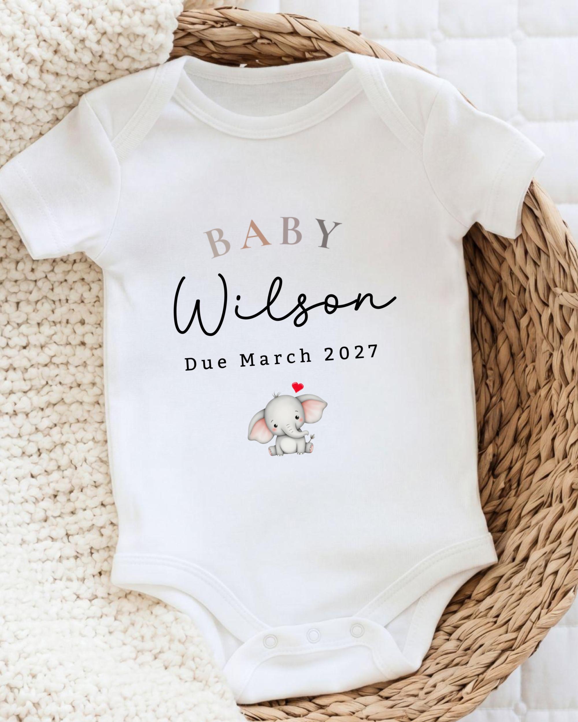 A white baby onesie with the text "BABY WILSON Due March 2027" printed on it, along with an illustration of a baby elephant.