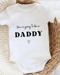 A white baby onesie with the text "You're going to be a DADDY" printed on it, along with a small heart symbol.
