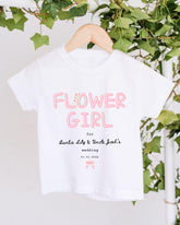 A white t-shirt with pink text and a date printed on it, hanging on a wooden hanger.