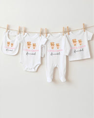 A row of baby clothes, including onesies and pajamas, hanging on a clothesline.