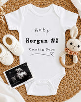 Baby clothing, baby shoes, a crocheted rabbit toy, and an ultrasound image are arranged on a woven mat.